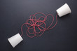 Two white paper cup connect with red rope used for classic phone on black stone table board. For old communication system concept