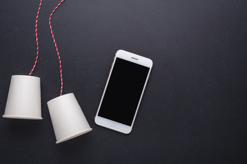 Two white paper cup connect with red rope used for classic phone and modern smartphone on black stone table board. For compare the old and new communication system concept