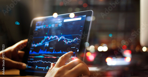 Fotomural Businessman checking stock market data on tablet on night background