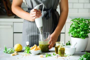 Woman using hand blender to make pesto. White kitchen interior design. Copy space. Vegetarian, clean eating lifestyle concept