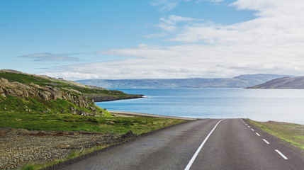 Wall Mural - Travel to Iceland. beautiful sunrise over the ocean and fjord in Iceland. Icelandic landscape with mountains, blue sky and green grass on the foreground. View of the road in the north-west of Iceland