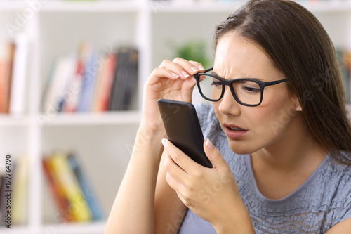 Cuadros en Lienzo Girl with eyesight problems trying to read phone text