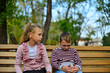 © andov - Brother and sister cuddling and sitting on a bench in a park on autumn day. Little girl and boy hugging