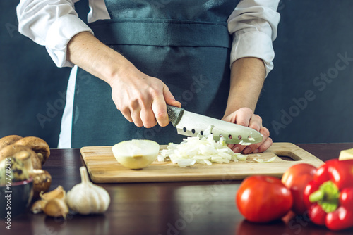 Zdjęcie XXL Szef kuchni w czarnym fartuchu wycina cebulę nożem. Koncepcja ekologicznych produktów do gotowania