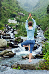 woman in yoga asana vrikshasana tree pose at waterfall outdoors