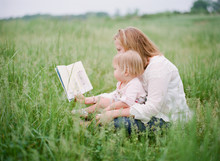 Mother And Daughter Reading A Story Book In A Field