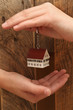 Eigenheim, Hausmodell in menschlichen Händen mit einem hölzernen Hintergrund