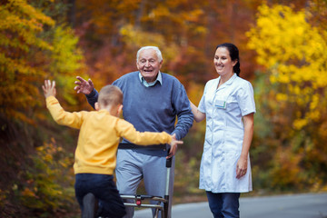 Cheerful disabled grandfather in walker welcoming his happy grandson