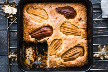 Pear seasonal cake in square black baking pan on dark rustic wooden table. Food photography concept