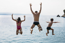 Daughter And Son With Father Jumping Together Into The Blue Sea