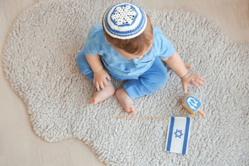 cute baby in kippah playing with dreidels while sitting on floor