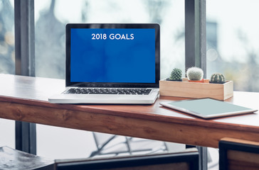 Poster - Goals for 2018 word in laptop computer screen with tablet on wood stood table in at window with blur background,Digital Business or marketing trending.