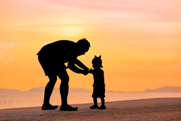 Silhouette father and son on beach in sunset time with twilight sky