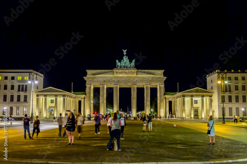 Платно Beleuchtetes Brandenburger Tor in Berlin bei Nacht im Sommer mit Passanten im Vo