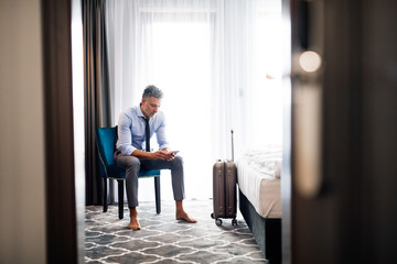 Wall Mural - Mature businessman with smartphone in a hotel room.