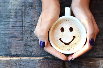 woman hands holding one cappuccino cup with optimistic face on wooden table