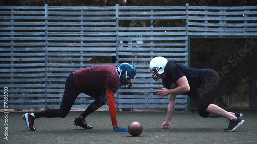 Zdjęcie XXL Dwóch hełmowanych piłkarzy w dwóch różnych mundurach pchanie obok siebie z ogrodzenia w tle