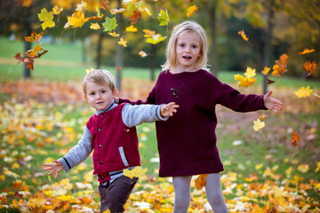 Sweet siblings, brother and sister, playing in the park with leaves