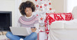 © Dash - Young woman purchasing Christmas gifts online as she sits cross legged on the floor in front of the decorated tree at home entering her credit card details on a laptop.