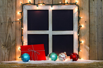 Wall Mural - Blank rustic window frame with string of holiday lights, snow, red envelope and colorful Christmas ornaments by antique aged wood background; black copy space 