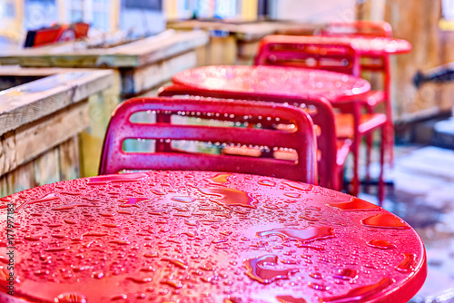 Fotografía Wet red table, chairs closeup outside restaurant sitting area by sidewalk during