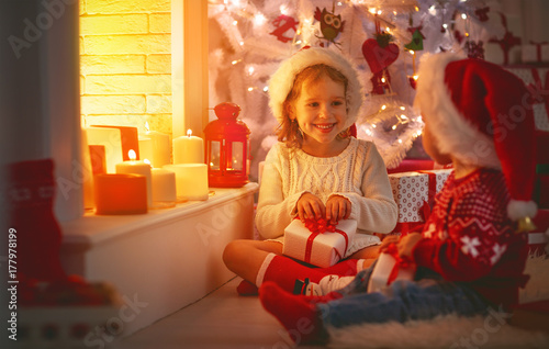 Plakat szczęśliwe dzieci z świątecznych prezentów w pobliżu choinki i kominka.