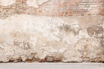 Wall Mural - Old weathered vintage brick wall with broken plaster and pavement on the ground. Grungy urban background.