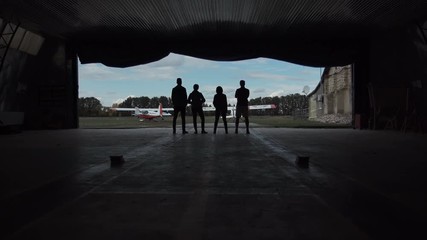 Wall Mural - Four people standing in an aircraft hangar silhouetted against the sky watching two small aircraft outside in a low angle view