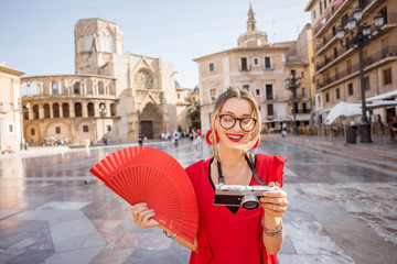 Wall Mural - Portrait of a young woman tourist in red dress with hand fan on the central square of the old town in Valencia city, Spain