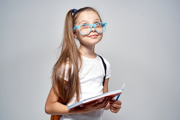 Wall Mural - little schoolgirl with glasses in hand notebook on gray background, study, school