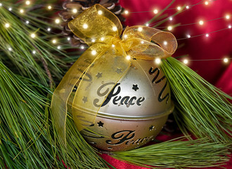 gold Christmas ornament with word peace and bow on pine with light string