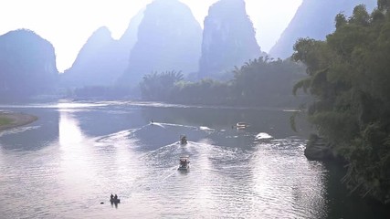 Wall Mural - Handheld shot of sunrise over landscape of Yangshuo, China. Boats floating in Li River in karst mountains top view. Travel, adventure and picturesque famous destination concept.