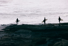 Surfers Silhouette On The Rocky Shore Of A Beach