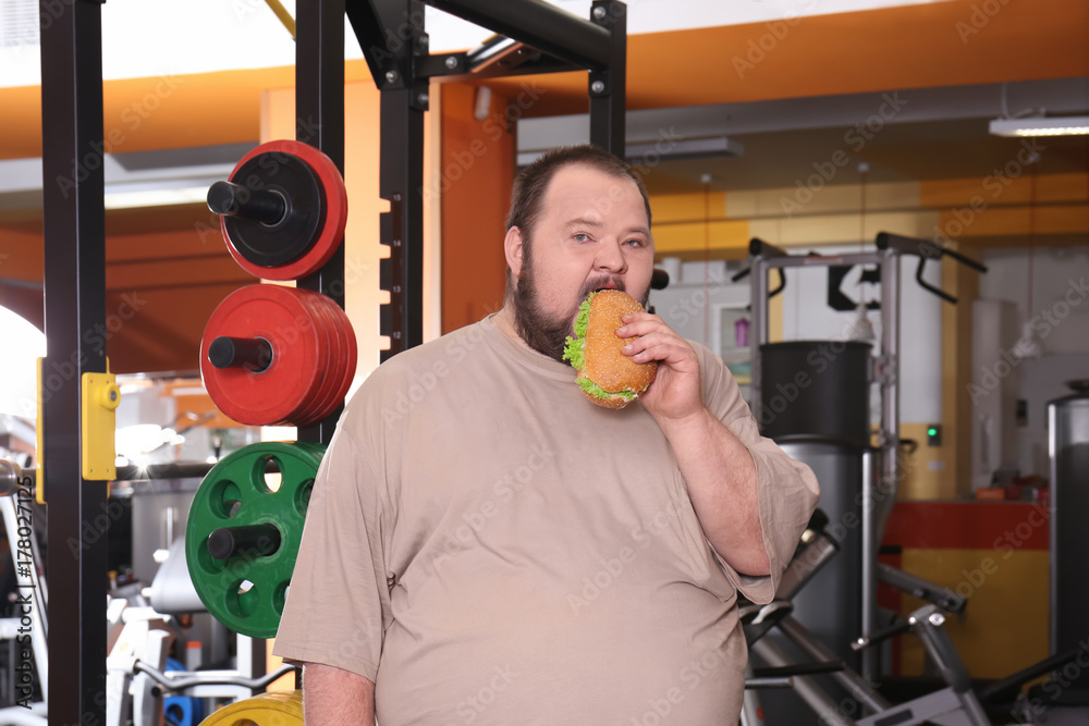 Overweight man eating sandwich in gym