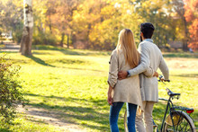 Back View Of Young Couple With Bicycle Walking In Park On Sunny Autumn Day.