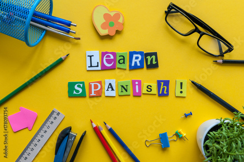Foto Word LEARN SPANISH made with carved letters on yellow desk with office or school supplies, stationery