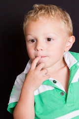 portrait of young boy hands in the mouth on black background