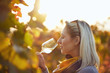 Portrait of a woman tasting white wine in autumn colorful vineyard