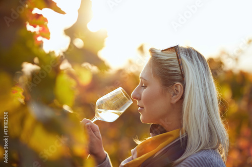 Fotografía Portrait of a woman tasting white wine in autumn colorful vineyard
