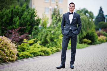 Portrait of a handsome young man in formal fancy suit posing on the pavement in the park on a prom day.