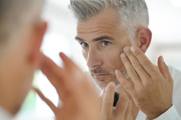 Middle-aged man applying cosmetic on his face, mirror view