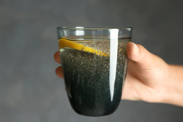 Hand holding glass of water with chia seeds and lemon on grey background