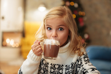 beautiful little blonde girl drinking cacao with marshmallow on christmas morning, looking at camera