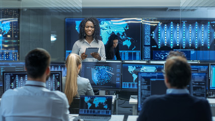 Wall Mural - Chief Project Engineer Consults Tablet Computer and Holds Briefing for a Team of Scientists that are Building Machine Learning System. Displays Show Working Model of Neural Network.