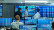 Three Experienced Stock Traders Talking Business, Consulting Documents and Argue About Data. They Work for a Big Stock Exchange Firm. Office is Full of Displays Showing Infographics and Numbers.