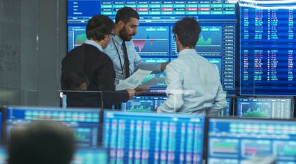 Aufkleber - Three Experienced Stock Traders Talking Business, Consulting Documents and Argue About Data. They Work for a Big Stock Exchange Firm. Office is Full of Displays Showing Infographics and Numbers.