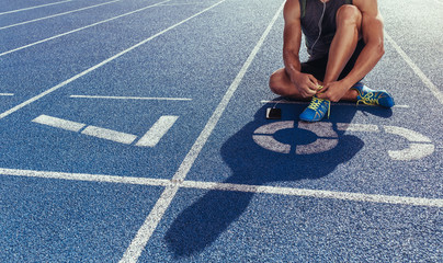 Wall Mural - sprinter tying shoe lace sitting on running track
