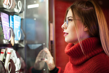 A Young Pretty Girl With Glasses Chooses A New Book In Vending Machines On The Street. Close-up.