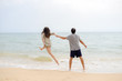 © gorosi - Adult young happy jumping couple on seashore outdoors nature sand background. Back view of pretty romantic lovers having fun holding hands in tenderness bliss moment. destination trip
