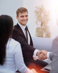 Two happy young men shaking hands while sitting at the office